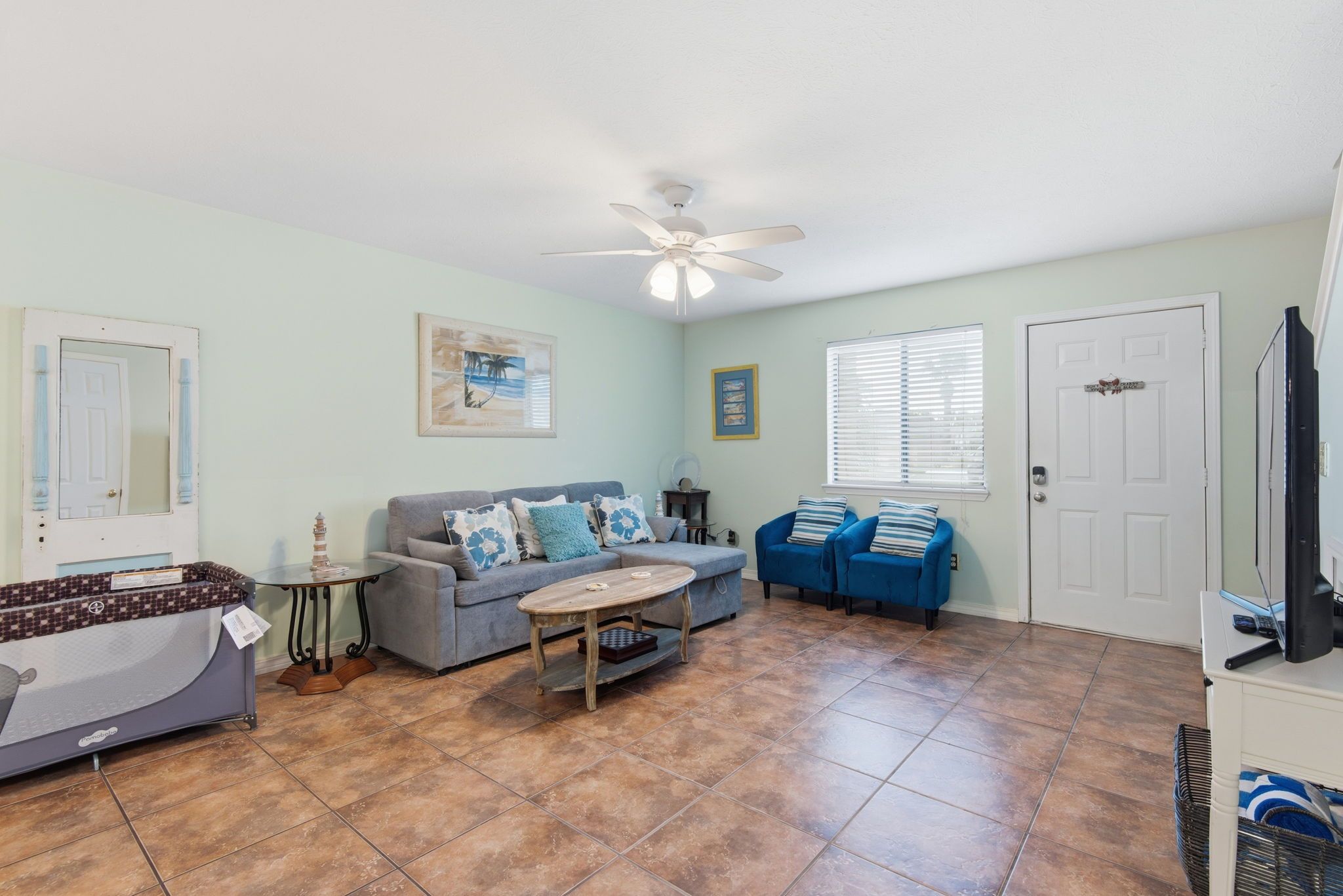 A living room with a grey sofa, a coffee table, a blue couch, a ceiling fan, and a television.