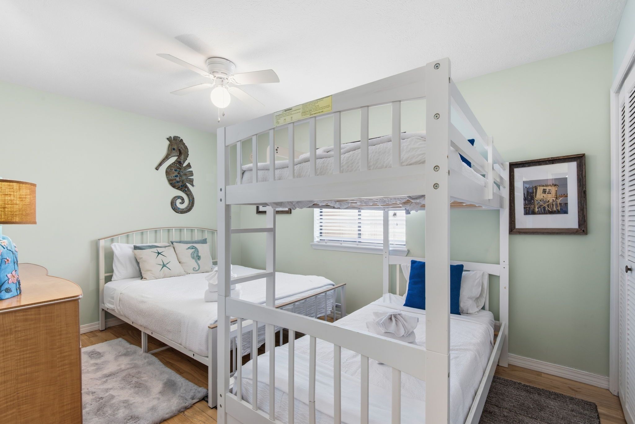 A bunk bed room with a ceiling fan, a seahorse wall decoration, and a framed picture on the wall.
