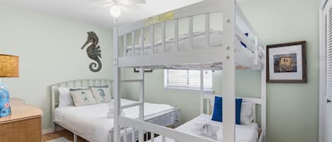 Une chambre avec des lits superposés, un ventilateur de plafond, une décoration murale représentant un hippocampe et un tableau encadré accroché au mur.