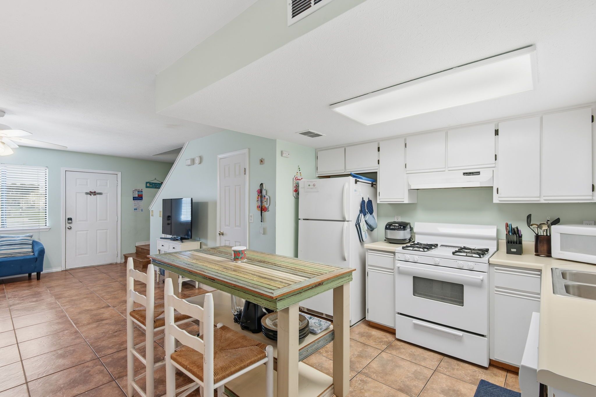 A kitchen with white cabinets, a stove, and a microwave. There is a dining table with chairs and a television in the corner.