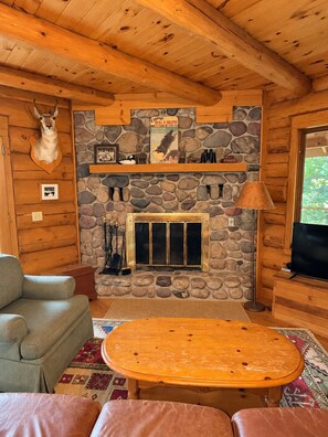 Ein Holzblockhaus-Interieur mit Kamin aus Stein, einem aufgehängten Tierkopf und einem Fernseher.