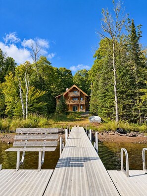 A wooden cabin with a balcony, surrounded by trees and a dock leading to a body of water. - Eagles Nest Lodge (Butternut)