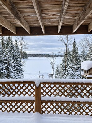 Une terrasse en bois, agrémentée d’une clôture à treillis, qui offre une vue sur un paysage enneigé, avec des arbres et une étendue d’eau.