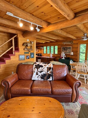 A wooden cabin interior with a leather sofa, a dining table, and a staircase. - Eagles Nest Lodge (Butternut)