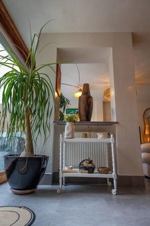 Uma sala de estar com uma planta em vaso, uma mesa consola branca com objetos decorativos e um vaso grande.