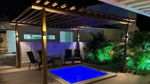 An outdoor swimming pool with a pergola overhead, surrounded by chairs and plants. - Mansion in Maracaipe, 100 meters from the sea, Jacuzzi, Swimming pool, Games room. (Ipojuca)