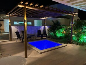Ein Freibad mit einer Pergola darüber, umgeben von Stühlen und Pflanzen.