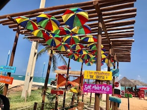 A beach area with multiple colorful umbrellas, wooden structures, and signs indicating beach activities. - Mansion in Maracaipe, 100 meters from the sea, Jacuzzi, Swimming pool, Games room. (Ipojuca)