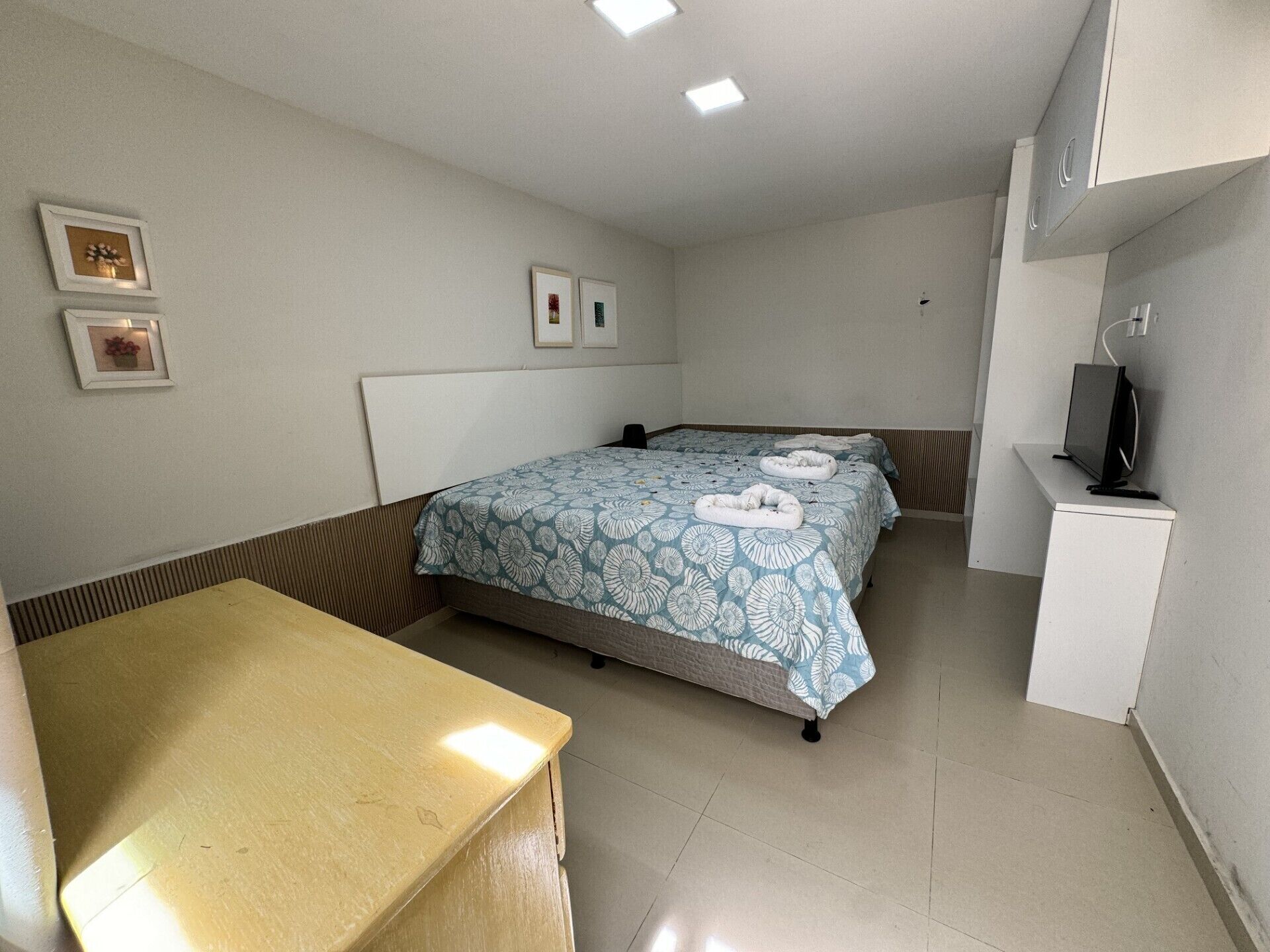 Una habitación de hotel pequeña con cama, escritorio, televisor y cuadros en la pared.
