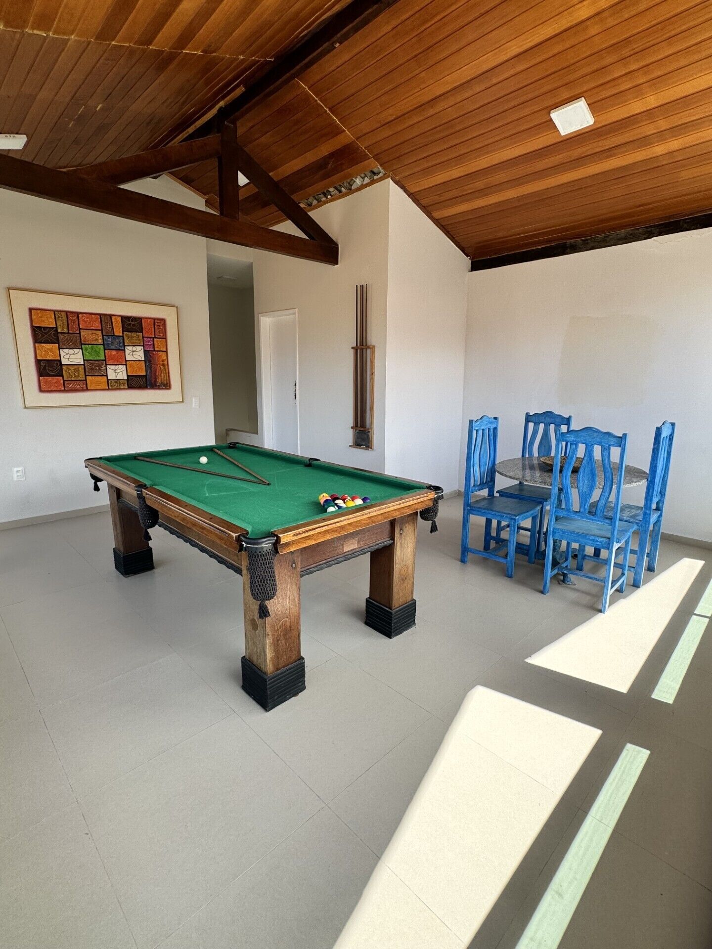 A pool table with a green felt surface, surrounded by blue chairs, in a room with a wooden ceiling and white walls.