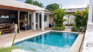 A swimming pool with a tiled deck, a covered outdoor seating area, and lush greenery. - Mansion in Maracaipe, 100 meters from the sea, Jacuzzi, Swimming pool, Games room. (Ipojuca)