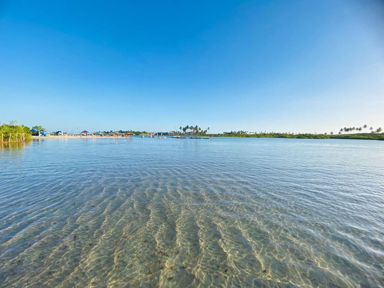 Una visuale limpida su un corpo d'acqua tranquillo, con una costa lontana, edifici e vegetazione.