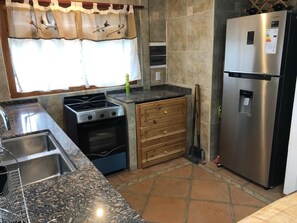 Una cocina con un refrigerador de acero inoxidable, estufa, pileta y un mueble de madera.