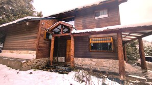 Eine Holzhütte mit Steinuntergrund, einer Holztür und einem Fenster mit Metallgitter.
