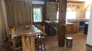 Ein Essbereich mit Holztisch und -stühlen, eine Küche mit Fliesenrückwand und ein Mülleimer.