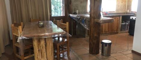 Un coin repas avec une table et des chaises en bois, une cuisine équipée d’une cuisinière et une poubelle.