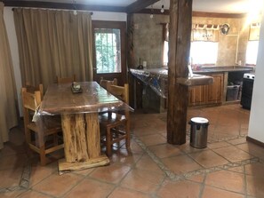 A dining area with a wooden table and chairs, a kitchen with a tiled backsplash, and a trash can. - Wonderful 3-bedroom house in Bariloche, Patagonia awaits you (San Carlos de Bariloche)