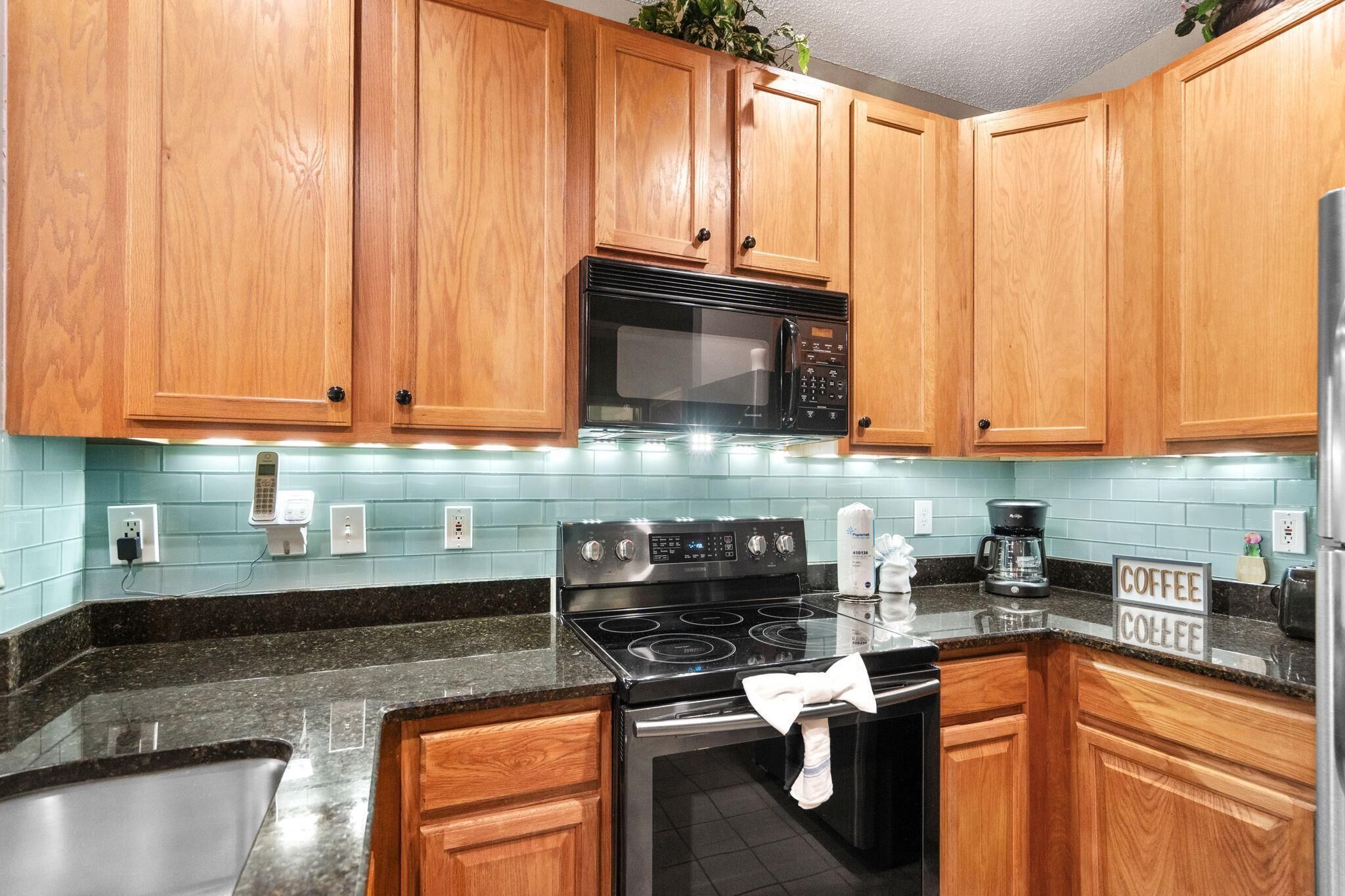 A kitchen with wooden cabinets, a black microwave, a stainless steel stove, and a sign that says 'Coffee Coffee.'