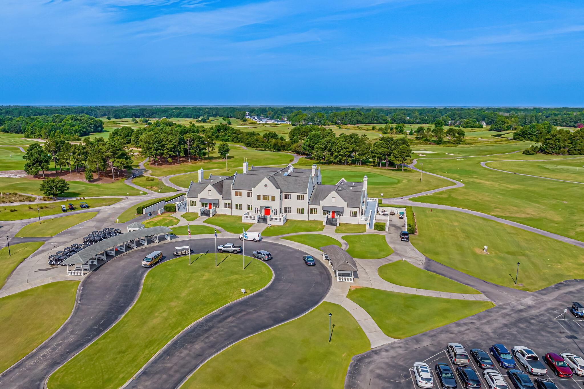 A golf course with a clubhouse, parking area, and surrounding greenery.