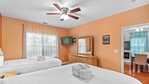 Ein Hotelzimmer mit zwei Betten, einem Deckenventilator, einer Holzkommode, einem Spiegel und einem Essbereich mit einem Stuhl.
