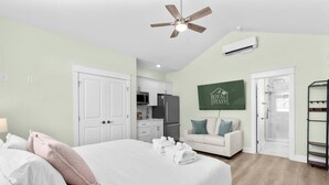 A bedroom with a bed, a ceiling fan, a kitchenette, a shower, and a green sign on the wall. - Riviera Suites Near Beach & Boardwalk (Myrtle Beach)
