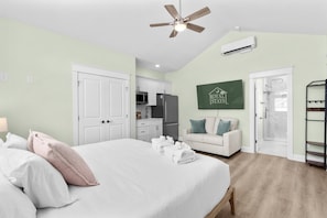 A bedroom with a bed, a ceiling fan, a kitchenette, a shower, and a green sign on the wall. - Riviera Suites Near Beach & Boardwalk (Myrtle Beach)