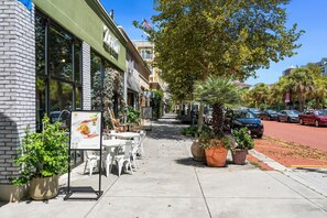 A sidewalk with outdoor seating, a brick building, and a tree. - Riviera Suites Near Beach & Boardwalk (Myrtle Beach)