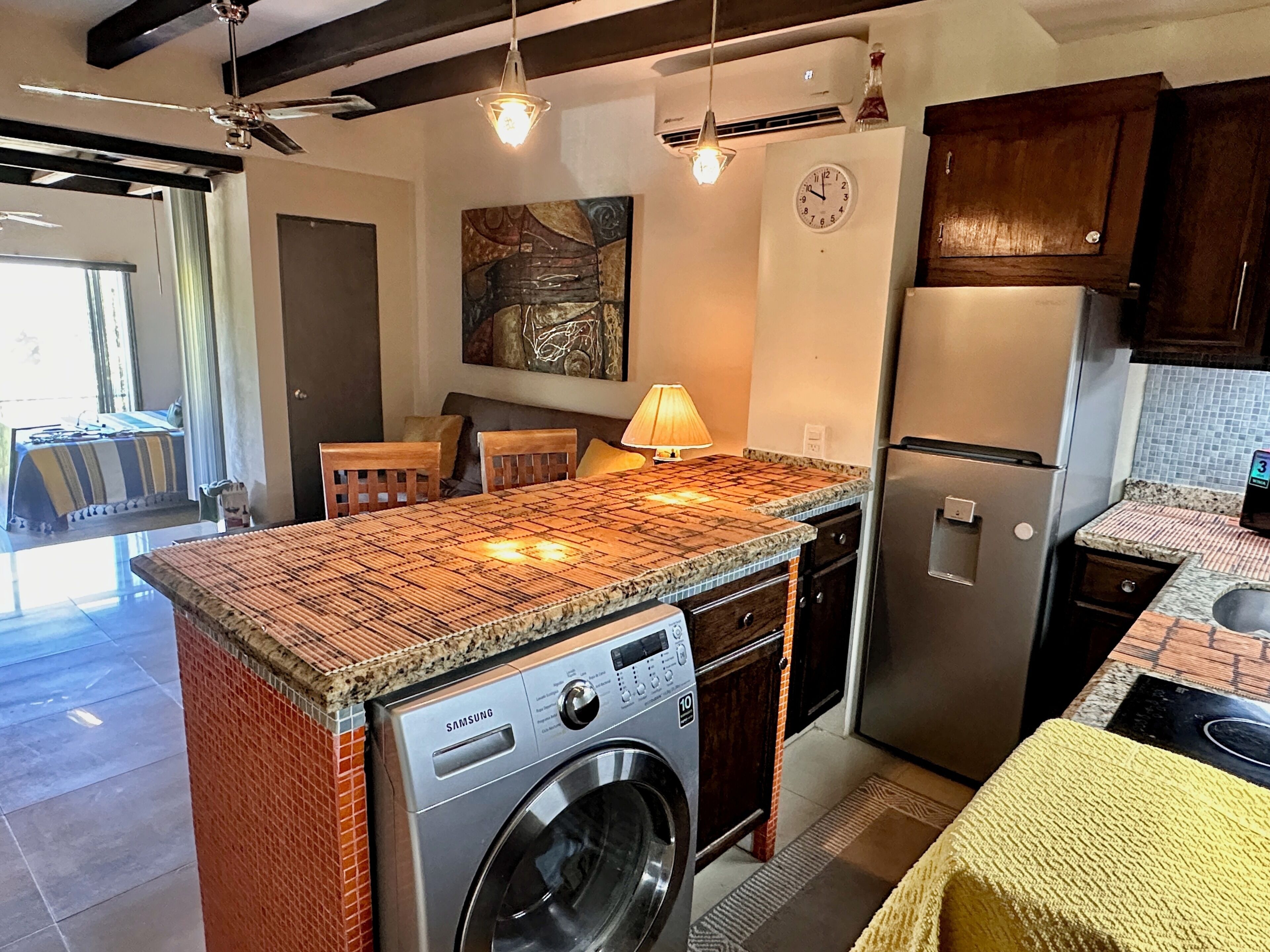 A kitchen with a built-in washing machine, a clock, and a dining area with a table and chairs.