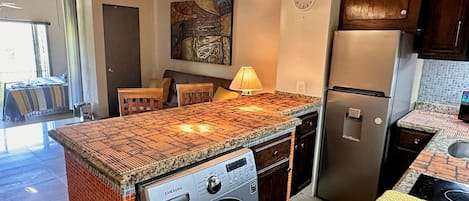 A kitchen with a built-in washing machine, a clock, and a dining area with a table and chairs.