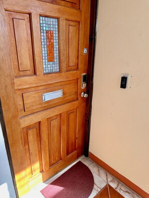 Eine Holztür mit Fensterglas, einem Briefschlitz, einem Klingelknopf und einer Fußmatte.