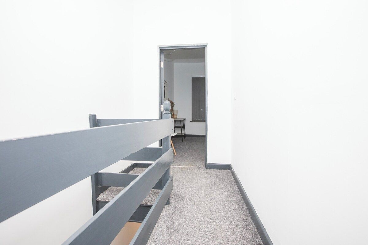 A narrow hallway with a grey railing, leading to a door at the end.