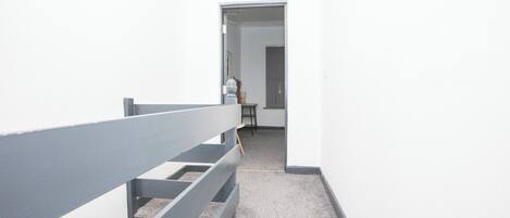 A narrow hallway with a grey railing, leading to a door at the end.