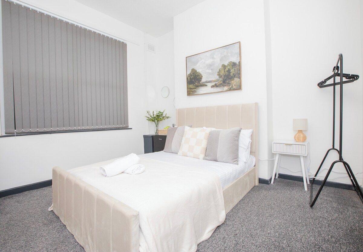 A hotel room with a bed, a bedside table, a lamp, a picture on the wall, and a floor lamp.