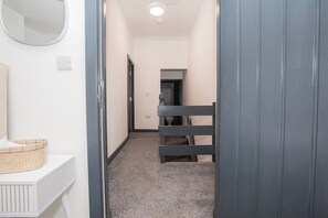 Ein schmaler Flur mit weißer Wand, einer hölzernen Bank und einer Tür zu einem weiteren Raum.