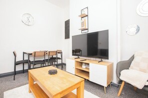 A modern living room with a flat-screen TV, wooden furniture, and a white wall with decorative elements. - Anfield City Stay | Shops & Transport | Parking (Merseyside)