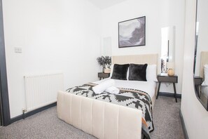 Ein Hotelzimmer mit Bett, Nachttisch, Spiegel und einem an der Wand hängenden Kunstwerk.