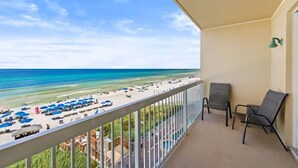 Een balkon met uitzicht op een strand, een zwembad en een terras met stoelen.