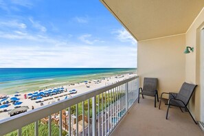Ein Balkon mit Blick auf einen Strand, ein Pool und eine Lounge mit Stühlen.