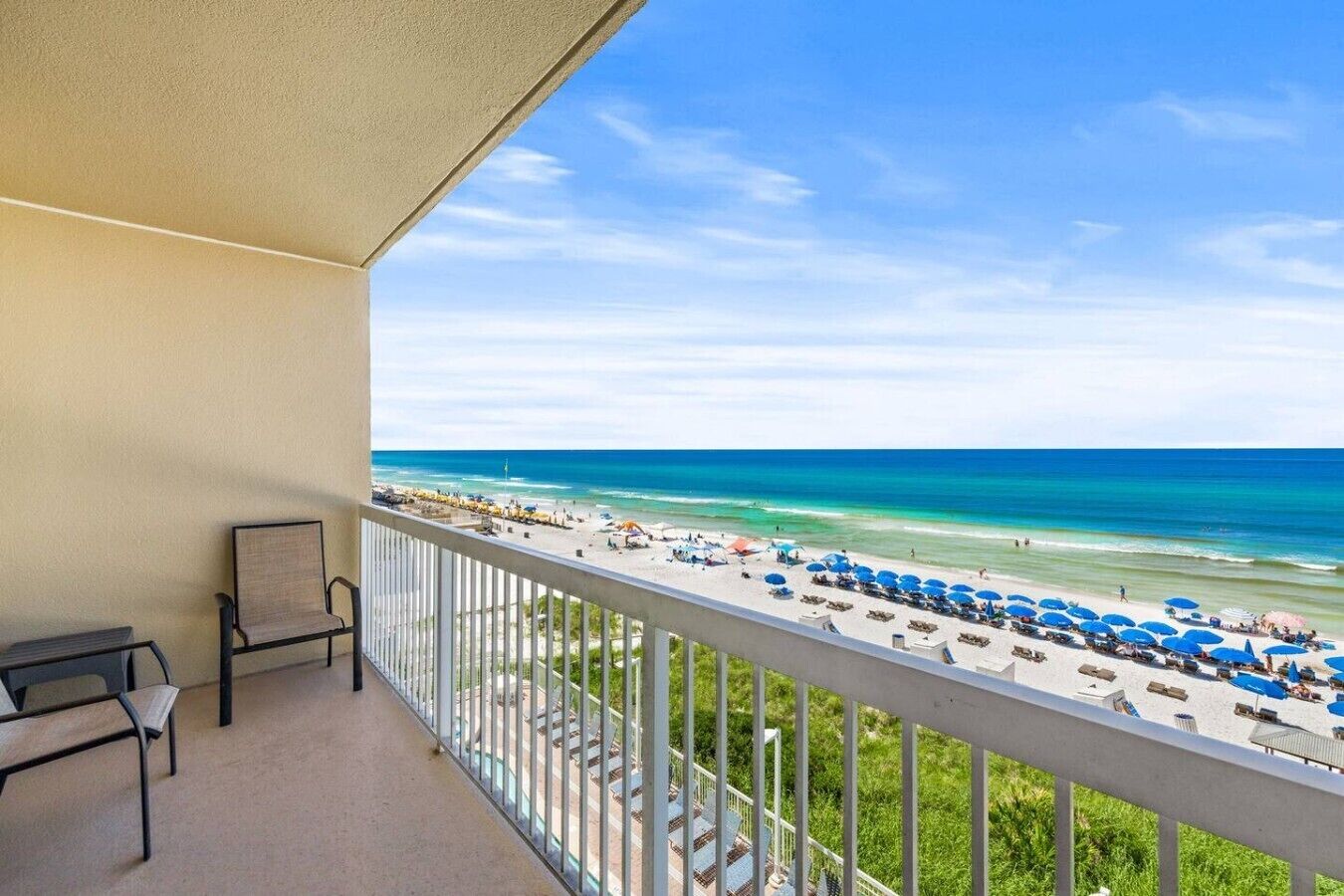 A balcony with a view of a beach, a chair, and a table.