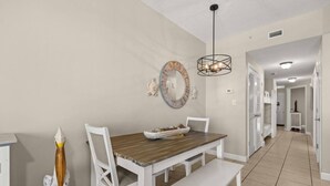Een eetgedeelte met een houten tafel, witte stoelen, een bank, een decoratieve spiegel en een hanglamp.