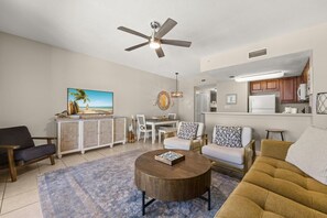 A living room with a ceiling fan, a television, a dining area, and a kitchen. - Seychelles Beachfront Condo | Gulf Views + Pools (Panama City Beach)