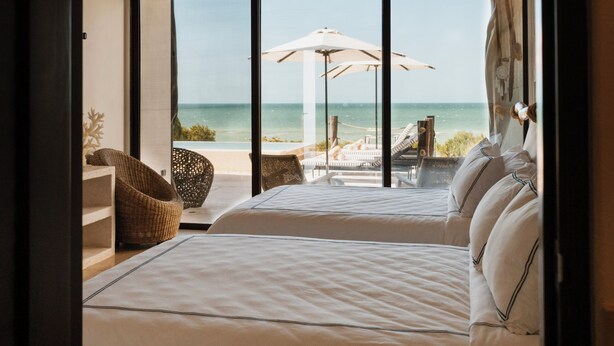 Un dormitorio con una cama grande, un ventilador de techo y vistas a la playa a través de amplios ventanales.