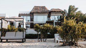 Una casa moderna frente a la playa con techo de paja, piscina y mobiliario de exterior.