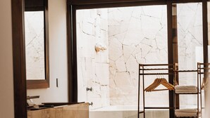 Un baño con tocador de madera, perchero y un ventanal con pared de piedra.