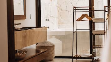 A bathroom with a wooden vanity, a hanging towel rack, and a large window with a stone wall.