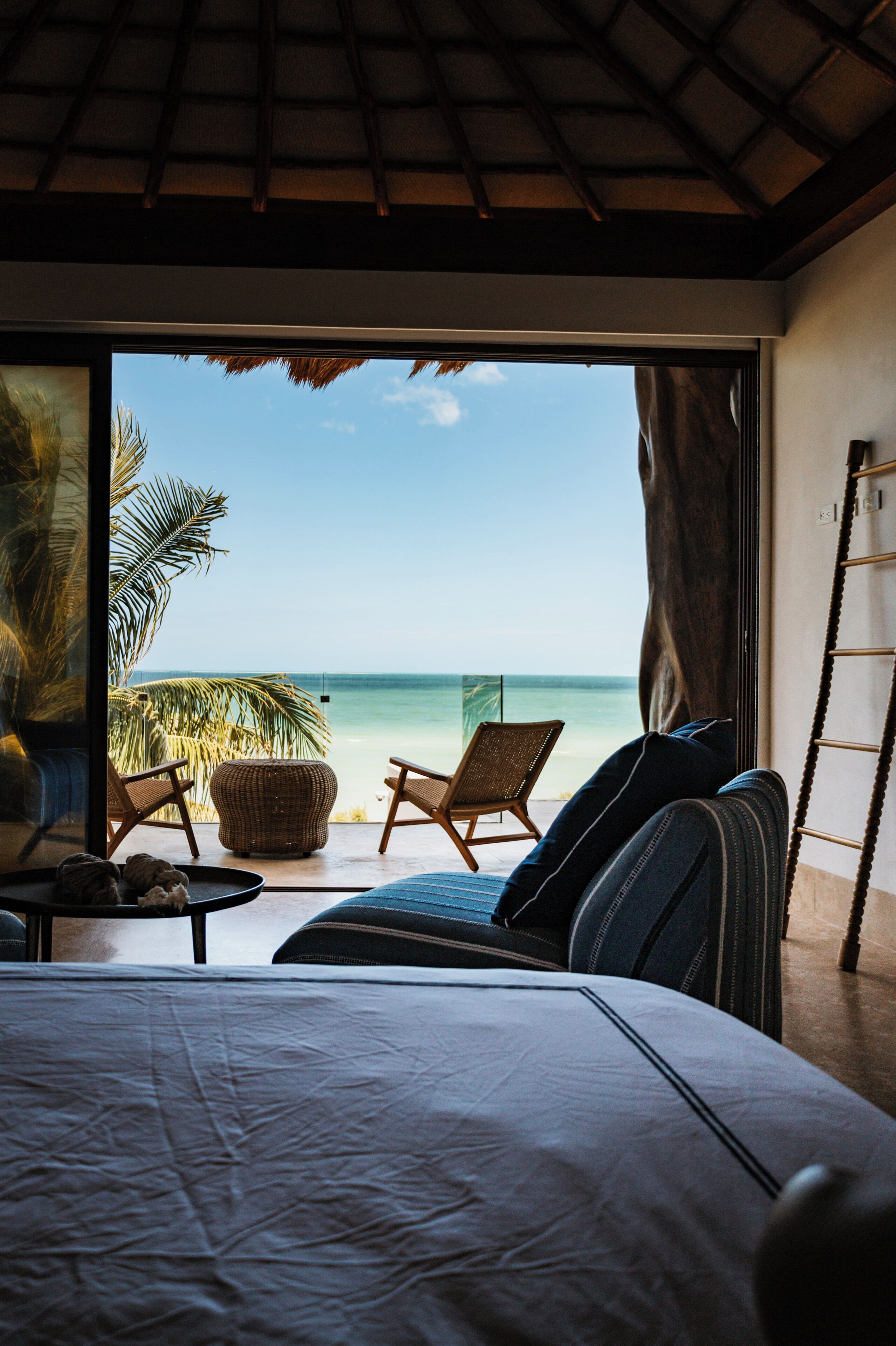Een slaapkamer met een groot bed, uitzicht op het strand en twee rieten stoelen.