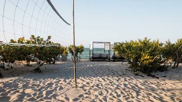 Une plage avec un filet de volley-ball, des chaises longues et une vue sur la mer.