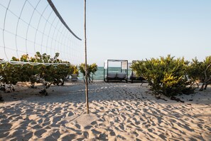 A beach with a volleyball net, lounge chairs, and a view of the sea.