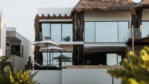 Un edificio moderno de dos pisos con amplios ventanales, techo de paja y mesas al aire libre.
