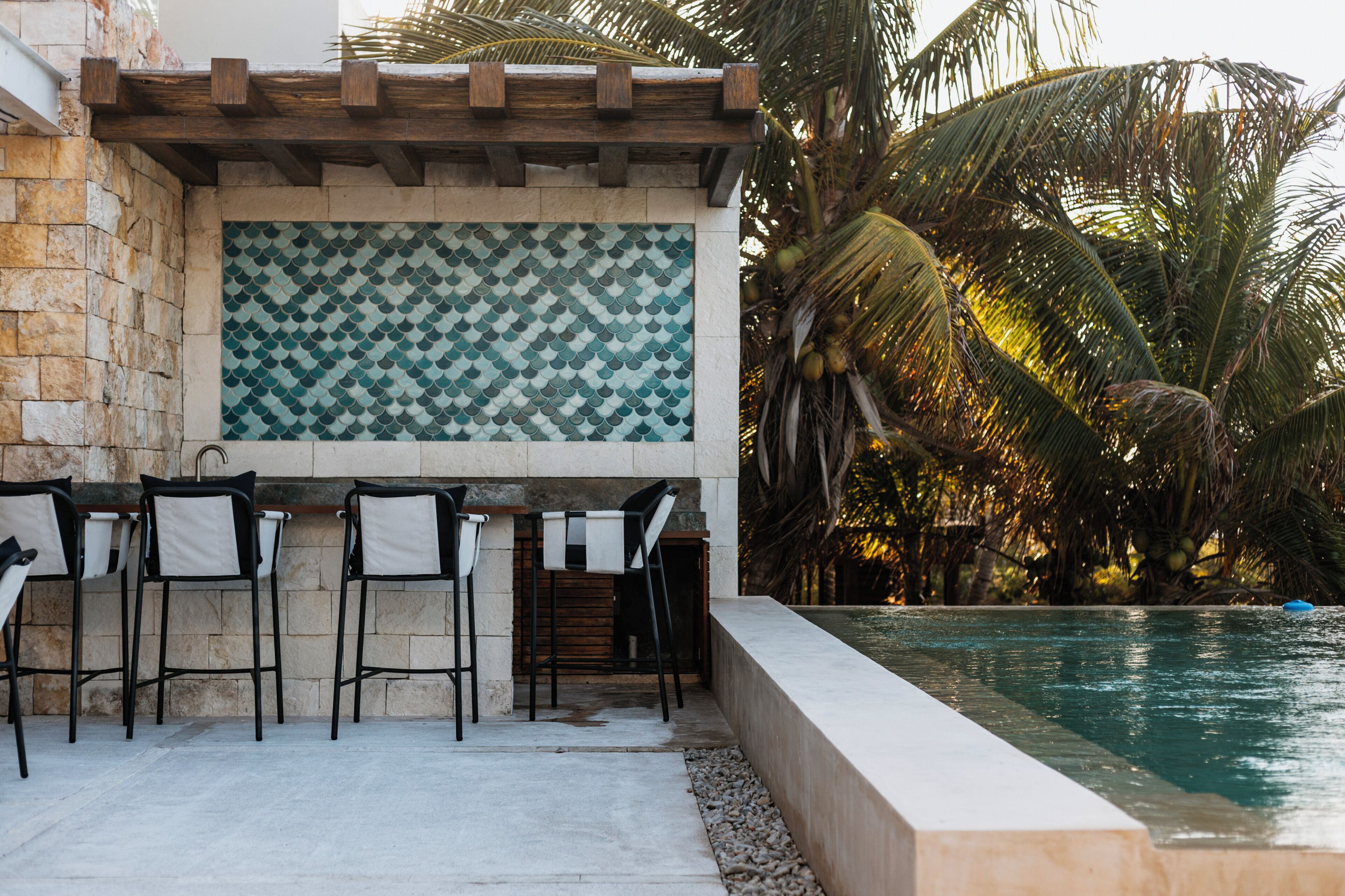 Un espace aménagé au bord de la piscine, avec un mur en pierre, un pare-feu en carrelage et trois tabourets de bar.